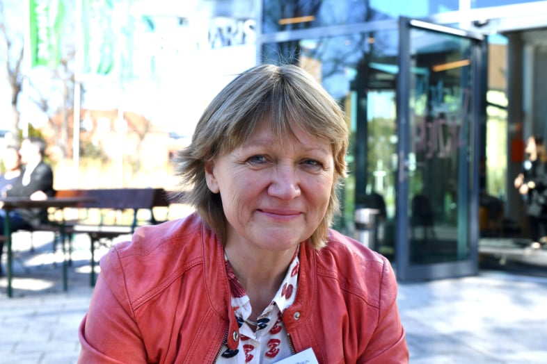 Sympathisch lächelnde Frau mit blonden gestuften mittellangen Haaren in hellroter Lederjacke schaut einen freundlich an. Portraitaufnahme